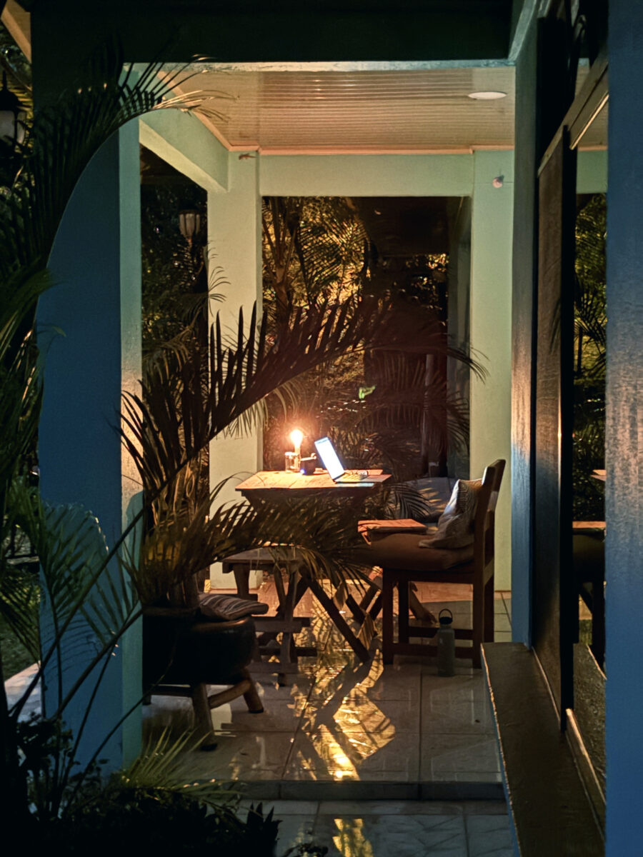 laptop and candle on an outdoor table against trees at night