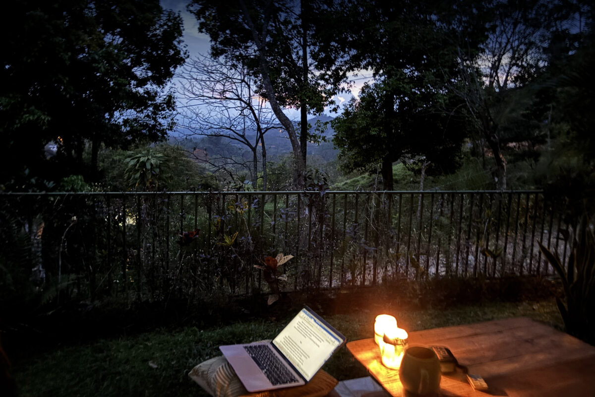 laptop and candle on an outdoor table against trees at night